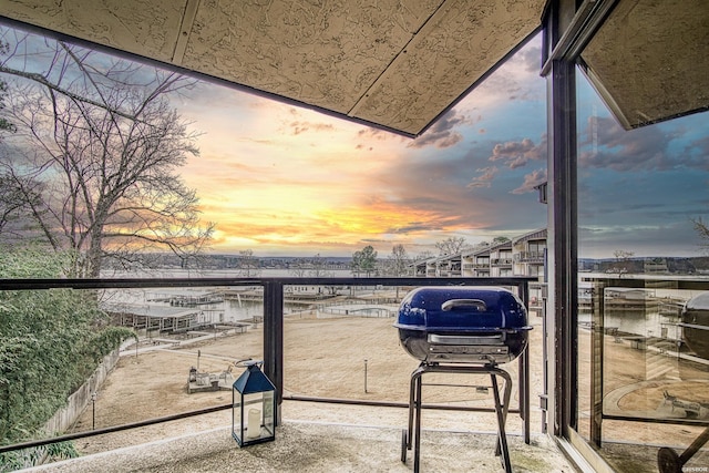 balcony at dusk featuring a water view and a grill