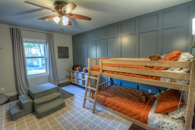 bedroom featuring ceiling fan, baseboards, and a decorative wall