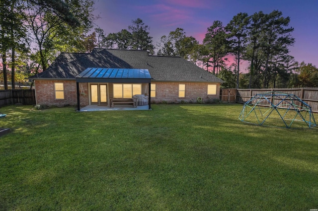 back of house at dusk with a patio area, a fenced backyard, a lawn, and brick siding