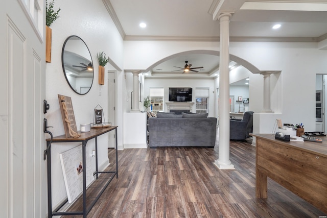 foyer with dark wood-style floors, crown molding, a fireplace, ceiling fan, and ornate columns