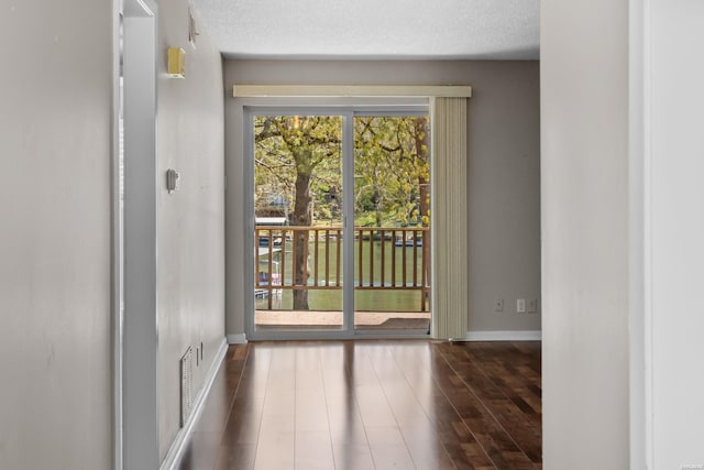 doorway with a textured ceiling, dark wood-style floors, visible vents, and baseboards