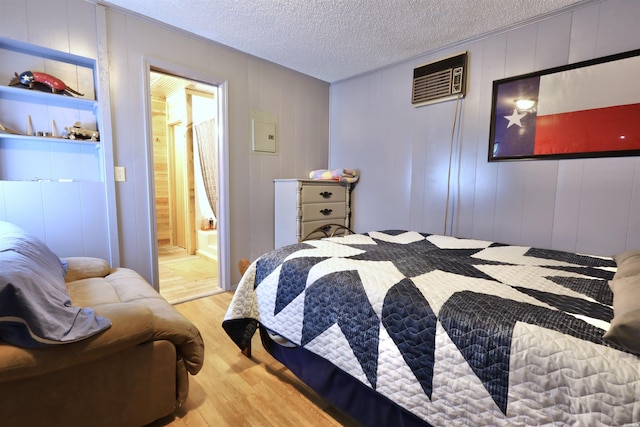 bedroom featuring a textured ceiling, a wall unit AC, wood finished floors, and ensuite bathroom