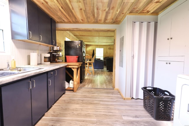 kitchen featuring a sink, wood ceiling, light wood-style floors, freestanding refrigerator, and washer / dryer