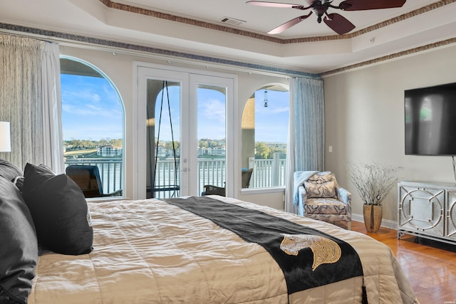 bedroom featuring a tray ceiling, access to outside, a water view, and visible vents