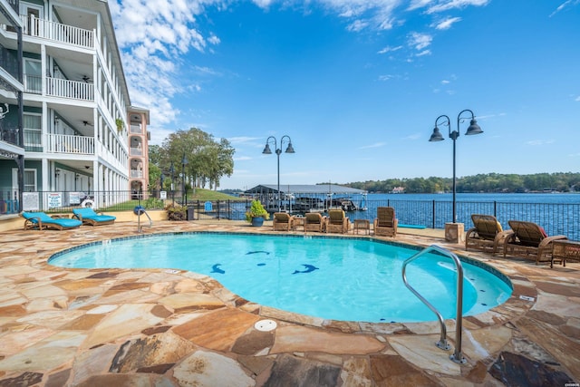 community pool featuring a patio area, a water view, and fence