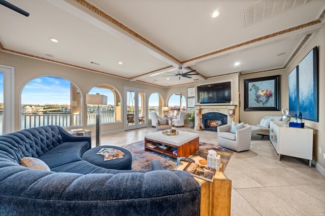 living area with a warm lit fireplace, baseboards, visible vents, a water view, and crown molding