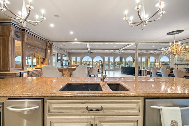 kitchen with ceiling fan with notable chandelier, light stone counters, a sink, and pendant lighting