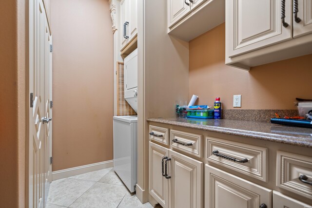 laundry area with light tile patterned floors, stacked washer / dryer, cabinet space, and baseboards