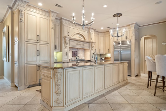 kitchen with hanging light fixtures, a kitchen island with sink, arched walkways, and cream cabinetry