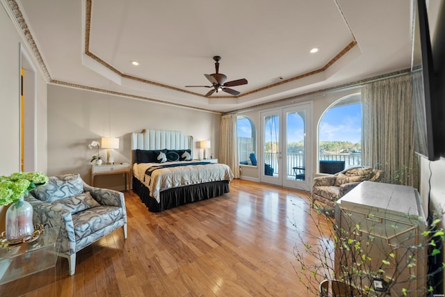 bedroom featuring access to exterior, a raised ceiling, and wood finished floors