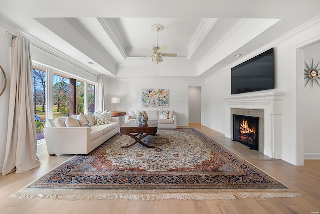 living area featuring a fireplace with flush hearth, crown molding, a tray ceiling, and wood finished floors