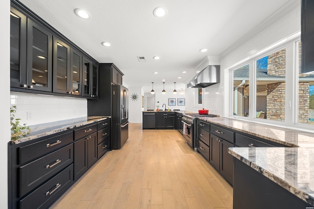 kitchen with visible vents, black appliances, light wood-style floors, wall chimney range hood, and light stone countertops