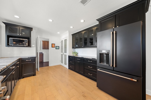 kitchen with light wood-type flooring, visible vents, high end fridge, washer / clothes dryer, and dark cabinetry