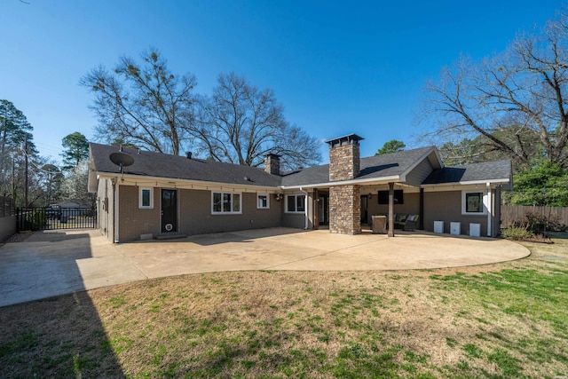 rear view of house featuring a lawn, fence, brick siding, a chimney, and a patio area