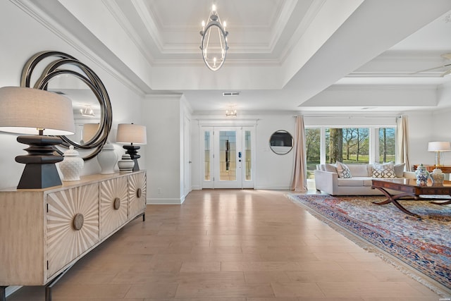 foyer entrance with visible vents, ornamental molding, wood finished floors, an inviting chandelier, and a raised ceiling