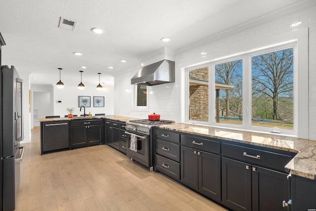 kitchen featuring visible vents, a sink, appliances with stainless steel finishes, a peninsula, and wall chimney range hood