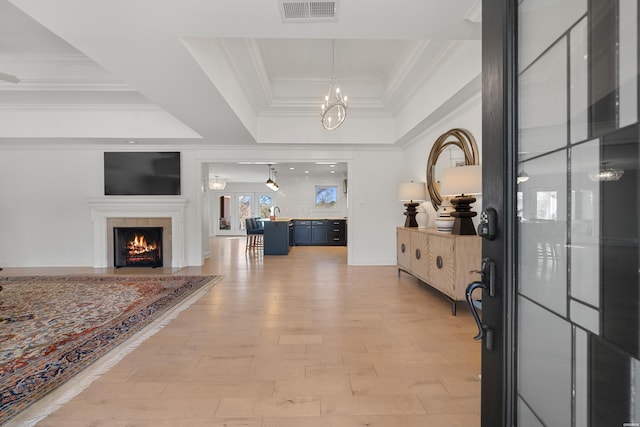 foyer featuring visible vents, a warm lit fireplace, crown molding, light wood-type flooring, and a raised ceiling