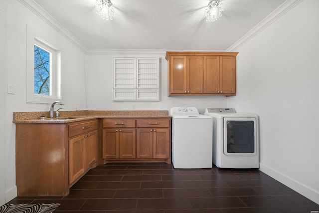 laundry area featuring crown molding, baseboards, separate washer and dryer, cabinet space, and a sink