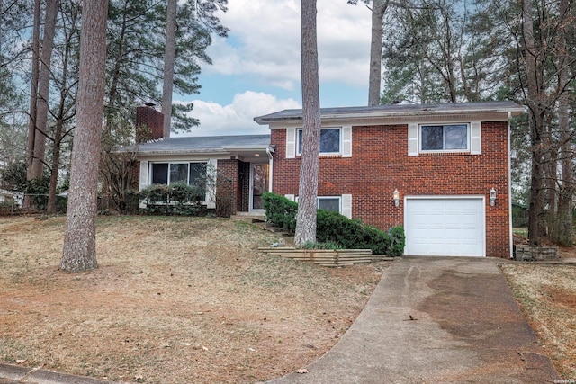 tri-level home with driveway, a garage, a chimney, and brick siding