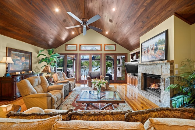 living area with ceiling fan, high vaulted ceiling, a stone fireplace, wooden ceiling, and wood finished floors