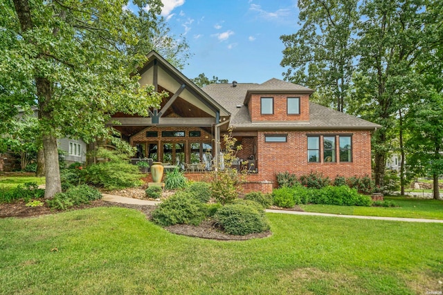 rear view of property featuring a shingled roof, brick siding, and a lawn