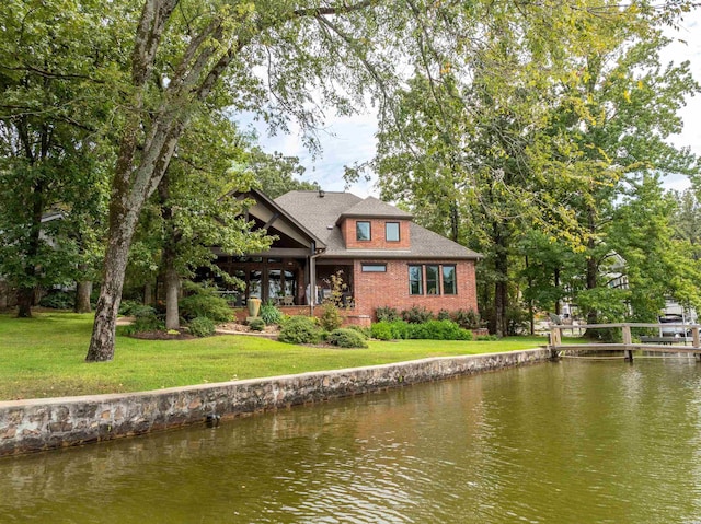 back of property featuring brick siding, a lawn, and a water view