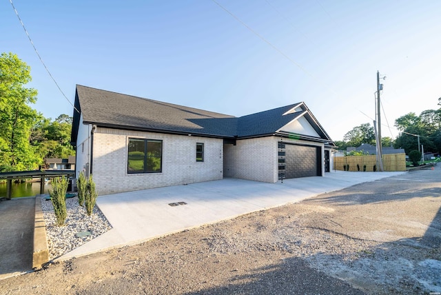 view of front of property featuring roof with shingles, brick siding, fence, a garage, and driveway