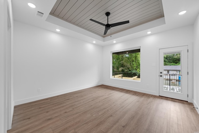 spare room with baseboards, visible vents, wood finished floors, a tray ceiling, and recessed lighting