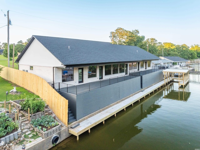 rear view of house with a water view, a shingled roof, and brick siding