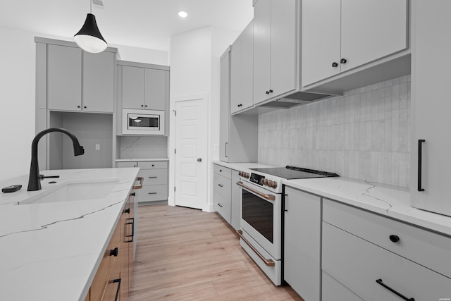 kitchen with white electric range oven, light stone counters, stainless steel microwave, decorative light fixtures, and a sink