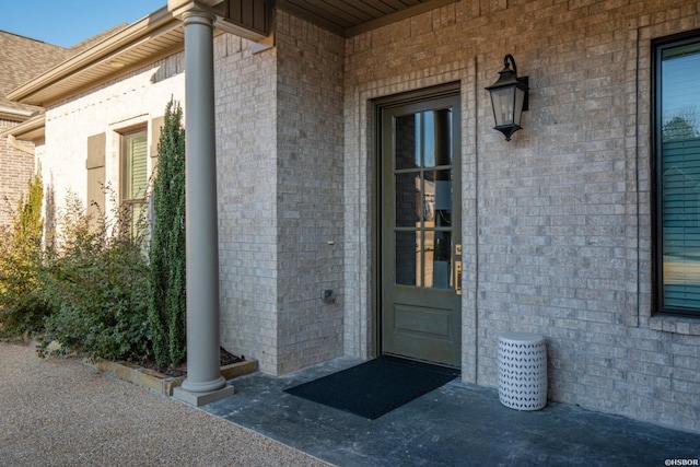 entrance to property featuring brick siding and roof with shingles