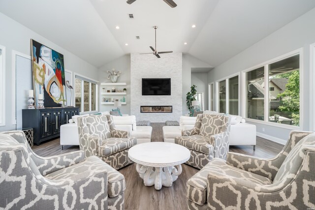 living room featuring wood finished floors, vaulted ceiling, a ceiling fan, and a stone fireplace