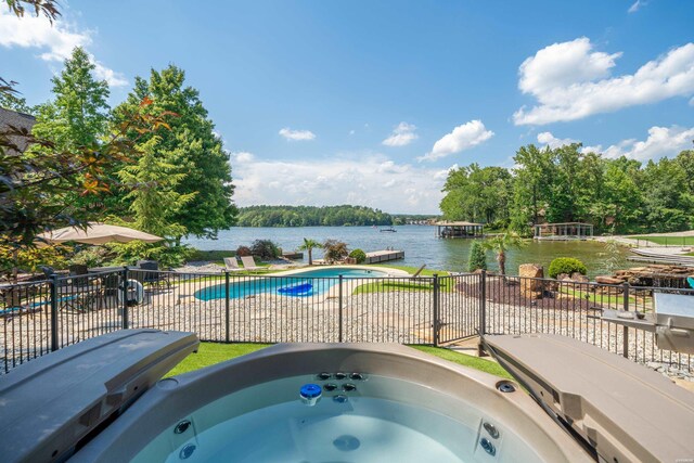 view of swimming pool featuring a water view, an outdoor hot tub, fence, and a fenced in pool