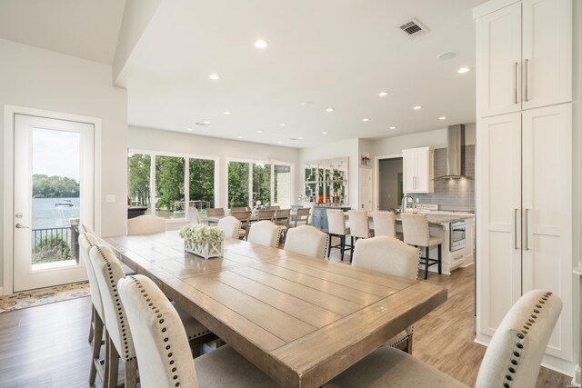 dining area featuring recessed lighting, a water view, visible vents, and light wood-style floors