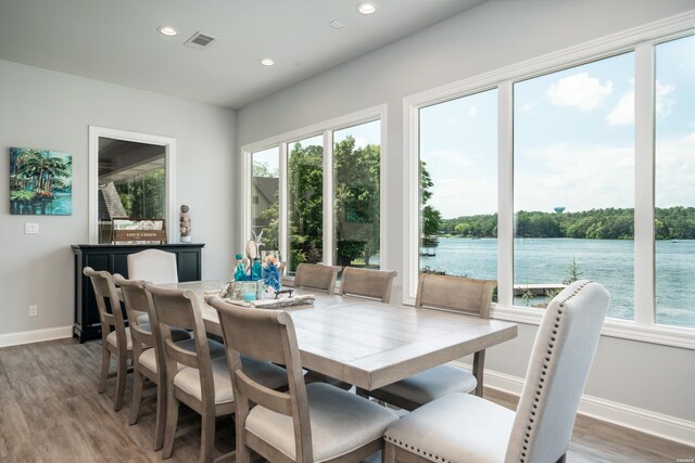 dining space featuring recessed lighting, a water view, visible vents, wood finished floors, and baseboards