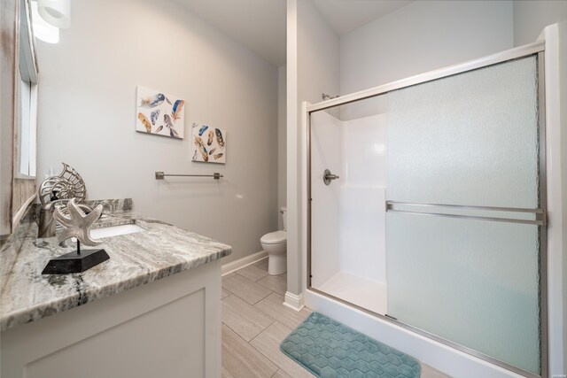 bathroom with wood finish floors, toilet, a shower stall, vanity, and baseboards