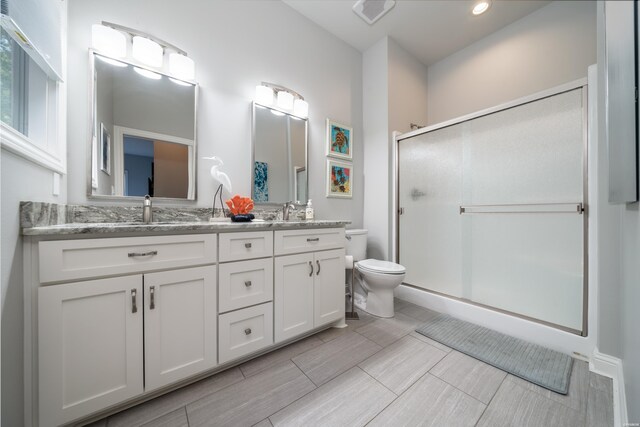 full bathroom featuring double vanity, a stall shower, visible vents, toilet, and a sink