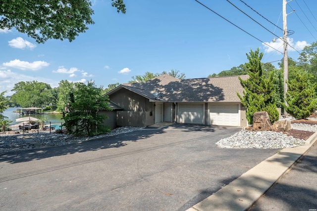 view of front of house featuring aphalt driveway, a water view, a shingled roof, and an attached garage