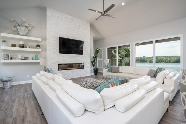 living area featuring light wood finished floors, a ceiling fan, vaulted ceiling, a stone fireplace, and baseboards