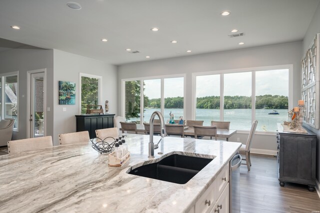 kitchen with light stone counters, white cabinetry, a sink, plenty of natural light, and a kitchen breakfast bar