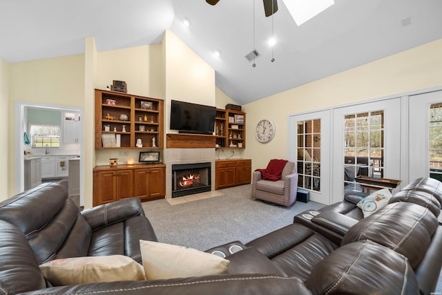 living area with light colored carpet, visible vents, a tiled fireplace, ceiling fan, and high vaulted ceiling