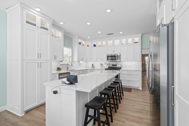 kitchen with light wood finished floors, white cabinets, a kitchen island, appliances with stainless steel finishes, and a kitchen breakfast bar