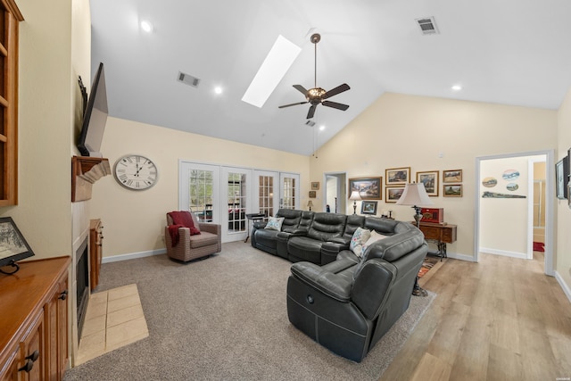 living room featuring high vaulted ceiling, a skylight, a tile fireplace, and visible vents