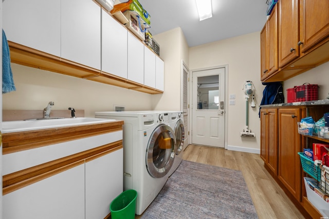 washroom featuring cabinet space, light wood finished floors, a sink, and washing machine and clothes dryer