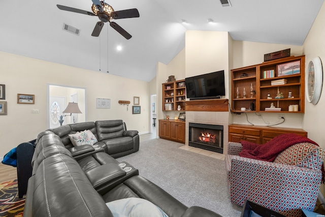 living area with light colored carpet, visible vents, a tiled fireplace, a ceiling fan, and high vaulted ceiling