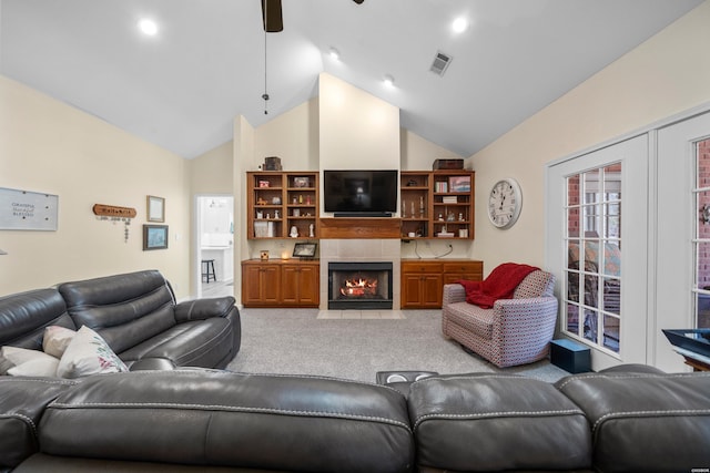 living area with light carpet, visible vents, a ceiling fan, a tiled fireplace, and high vaulted ceiling