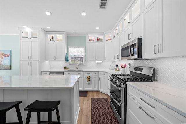 kitchen with stainless steel appliances, visible vents, white cabinetry, a sink, and a kitchen bar