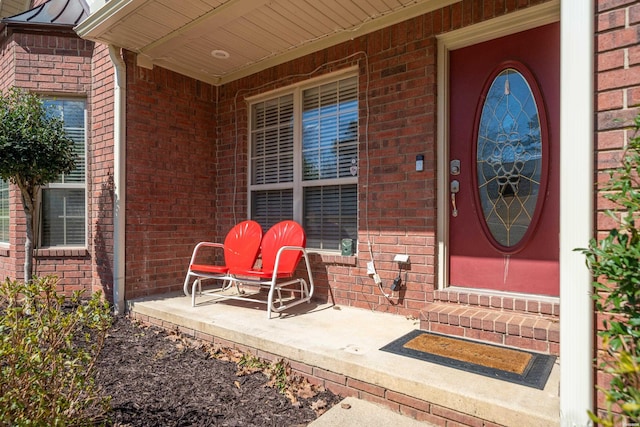 view of exterior entry featuring a porch and brick siding