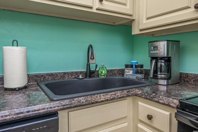 kitchen featuring cream cabinetry, dark countertops, dishwasher, and a sink