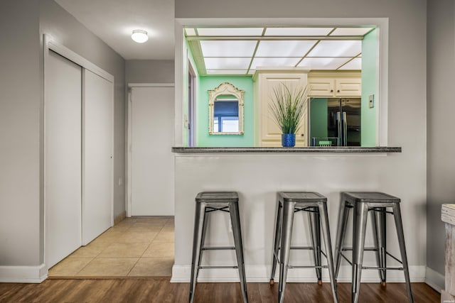 kitchen featuring tile patterned floors, a kitchen breakfast bar, black fridge, and baseboards
